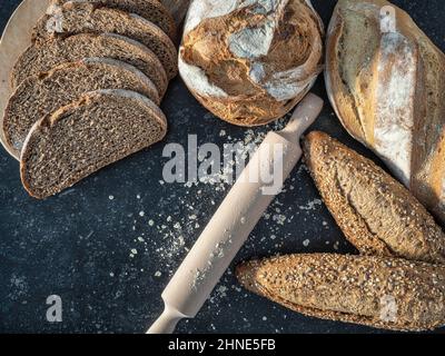 Panini freschi, pane integrale, pasta madre e pane tagliato con un mattarello e farina. Su sfondo nero di granito rustico. Spazio per la copia. Foto Stock