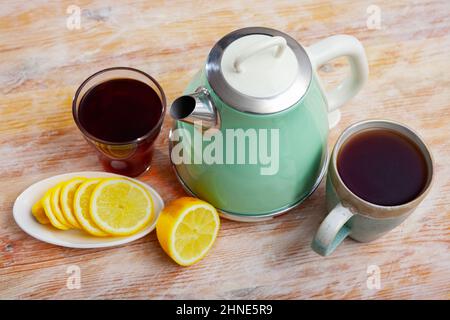 bollitore elettrico, due tazze di tè e limone a fette Foto Stock