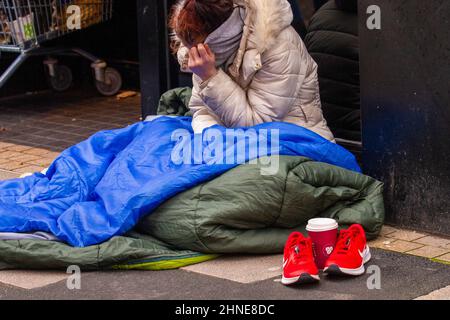 Donna senzatetto che dorme rude con le sneaker rosse Nike e la tazza di caffè Costa a Preston, Regno Unito Foto Stock