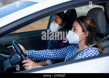 Due donne in maschere protettive in un abitacolo auto Foto Stock
