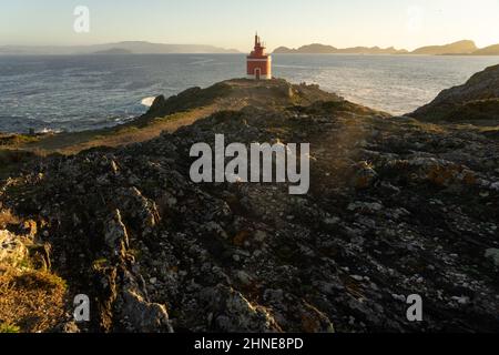 Faro rosso Punta Robaleira a Capo di Home al tramonto nella zona di Rias Baixas sulla costa della Galizia con le isole Cíes sullo sfondo. Foto Stock