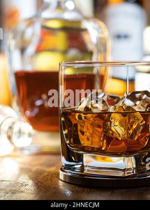 Bicchiere di whisky sulle rocce su una barra di legno con bottiglie sullo sfondo Foto Stock