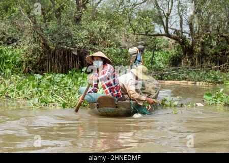 Pescatori vietnamiti che schiariscono giacinto d'acqua (Eichhornia crassipes (Mart) Solms) dalle loro reti da pesca sul fiume Mekong, Delta del Mekong, Vinh Long Foto Stock