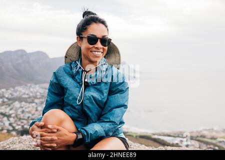 Ritratto di una donna sorridente escursionista che indossa occhiali da sole seduti su una roccia e rilassante Foto Stock