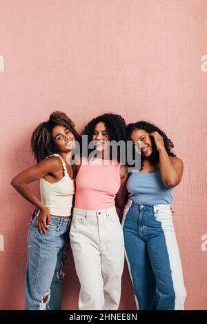 Gruppo di tre amici femminili che appoggiano la parete rosa indossando abiti casual luminosi Foto Stock