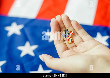 Primo piano della giovane donna che tiene in mano il perno della croce cristiana. Bandiera americana sullo sfondo. Concetto di patriottismo e diritti religiosi. Foto Stock