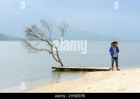 Un uomo vietnamita in un cappello conico si trova presso la laguna di Lap An, la baia di Lang Co (vicino a Hue), il distretto di Phu Loc, la provincia di Thua Thien Hue, il Vietnam centrale Foto Stock