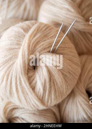 Immagine estetica di matassa di filato leggera e ariosa beige. Vista ravvicinata del filo soffiato di spessore medio in alpaca e lana merino. Aghi da maglieria bloccati in matassa di filato. Spazio di copia Foto Stock