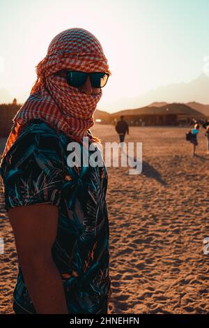 Hurghada Egitto Gennaio 2022 Ritratto verticale di un uomo attraente in piedi nel deserto in un villaggio vicino a hurghada. Bagliore del sole durante il tramonto h Foto Stock