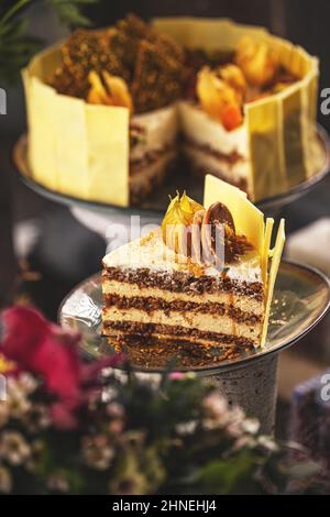 Fetta di torta a strati di noci con crema di mascarpone decorata con bacche d'oro e biscotti Foto Stock