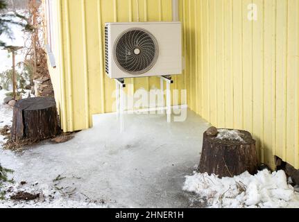 Aria condizionata macchina all'aperto su rack casa domestica parete gialla. Molto ghiaccio sotto di esso in freddo giorno d'inverno. Foto Stock