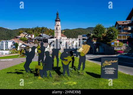 Statue dei musicisti Kastelruther Spatzen all'inizio della città Kastelruth, la chiesa Pfarrkirche si erge fuori dalle case. Foto Stock