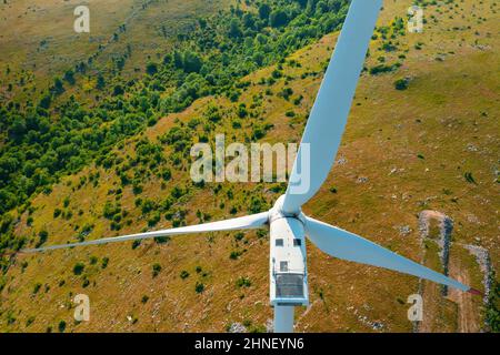 La turbina eolica con elica di grandi dimensioni genera elettricità in rotazione presso la stazione in altopiano coperto da alberi verdi e vista aerea ravvicinata Foto Stock