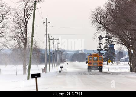 Scuolabus viaggiando lungo una strada di campagna con nevicate e neve soffiata in inverno Foto Stock