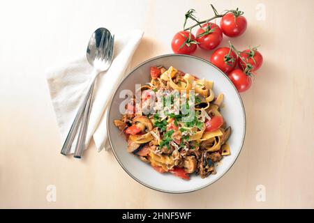 Tagliatelle con salsa di carne tritata, pomodori e verdure con parmigiano e prezzemolo guarnire su un piatto e un tavolo di legno chiaro, spazio copia, hi Foto Stock