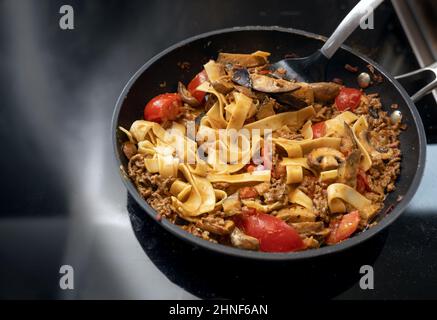 Padella di tagliatelle e salsa bolognese con carne macinata, pomodori e verdure sul piano cottura nero, spazio copia, fuoco selezionato, stretto Foto Stock