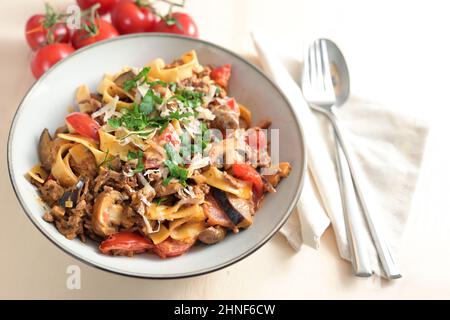 Piatto di pasta, tagliatelle e salsa di carne tritata, pomodori e verdure con parmigiano e prezzemolo guarnire su un piatto e un tavolo di legno chiaro, cop Foto Stock