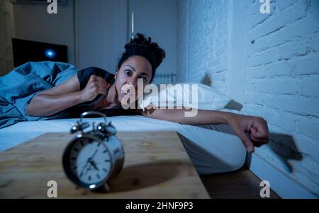 Insonnia e disperata bella afro americana donna svegliarsi di notte non in grado di dormire guardando l'orologio che soffre di insonnia in disturbi del sonno e. Foto Stock