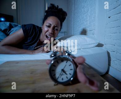 Insonnia e disperata bella afro americana donna svegliarsi di notte non in grado di dormire guardando l'orologio che soffre di insonnia in disturbi del sonno e. Foto Stock