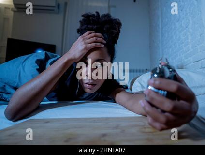 Insonnia e disperata bella afro americana donna svegliarsi di notte non in grado di dormire guardando l'orologio che soffre di insonnia in disturbi del sonno e. Foto Stock