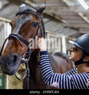 Teenage ragazza cavallo rider regolare le redini in imbracatura alla scuderia Foto Stock