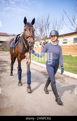 Giovane ragazza di jockey che cammina con il cavallo prima di allenarsi Foto Stock