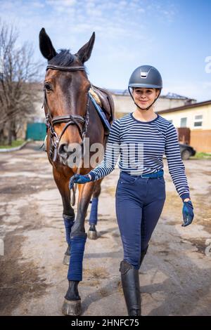 Giovane ragazza di jockey che cammina con il cavallo prima di allenarsi Foto Stock