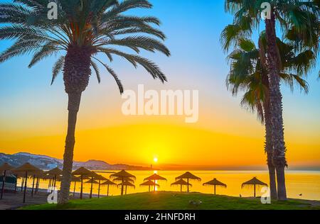 Goditi un'idilliaca spiaggia di Malagueta con alte palme e ombrelloni di paglia di fronte alla costa, Malaga, Spagna Foto Stock