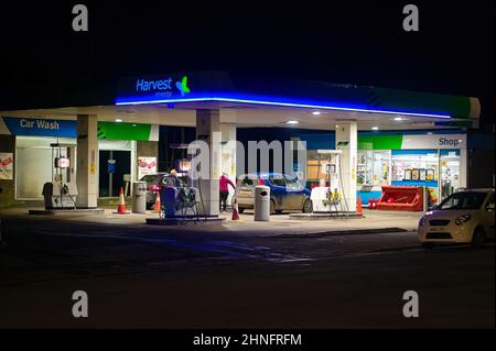 Un distributore di benzina Harvest di notte sulla High Street con una donna che riempie un'auto. Foto Stock