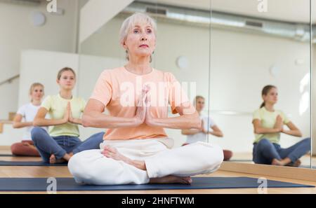Persone di diverse età seduti in posizione lotus praticare meditazione in classe yoga Foto Stock