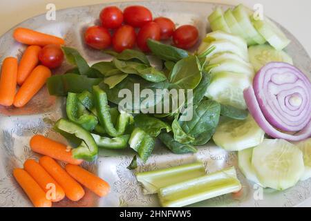 Un piatto d'argento che offre spinaci biologici crudi, cetrioli, pomodori a susina, colorati, a misura di snack, cipolla rossa, carote per bambini, sedano e peperoni verdi Foto Stock