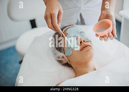 Primo piano ritratto delle mani di estetista applicazione di una maschera di alginato sul volto di una donna adulta. Cura del corpo Spa. Bellezza naturale. Trattamento di ringiovanimento Foto Stock