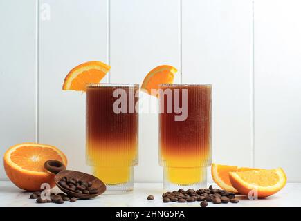 Caffè nero americano ghiacciato e strato di succo di arancia e limone decorato con arance a fette e fagioli di caffè. Menu di concetto per la caffetteria Foto Stock