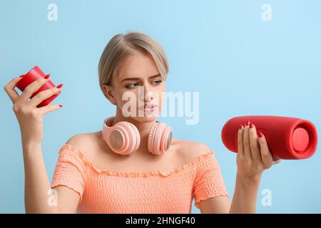 Donna con cuffie moderne che sceglie l'altoparlante wireless portatile su sfondo blu Foto Stock