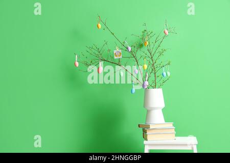 Pila di libri, vaso con rami d'albero e uova di Pasqua su stool stepladder vicino muro di colore Foto Stock