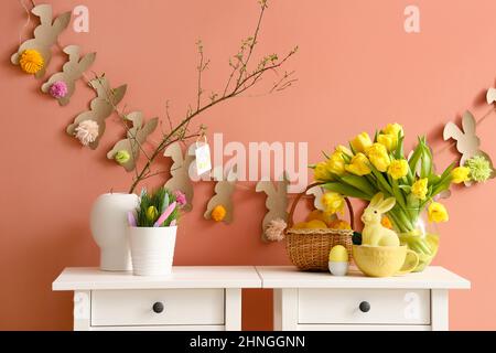 Vaso con rami d'albero, tulipani belli e decorazioni pasquali su tavoli vicino a pareti colorate Foto Stock