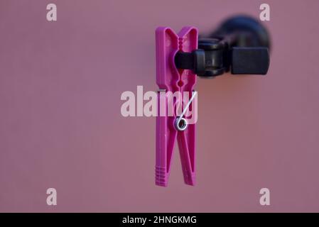 Vintage fucsia clothespin agganciato su un cane nero otturatore contro una parete rosa pallido di stucco a Nafplio, Grecia. Foto Stock