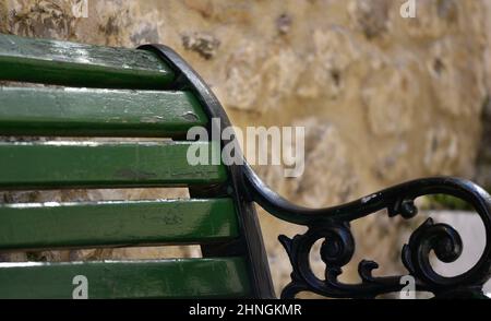 Vecchia panca rurale in legno verde pino con un braccio in ferro battuto lavorato a mano contro un muro di pietra a Nafplio, Grecia. Foto Stock