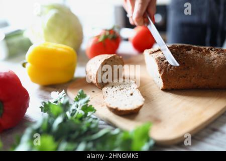 Le mani femminili tagliano il pane sul tavolo da cucina Foto Stock