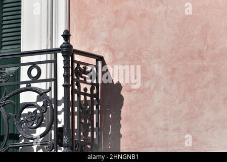 Vecchia facciata neoclassica casa con persiane di legno verde pino e un balcone con ringhiera in ferro battuto artigianale su una parete di stucco veneziano rosa pallido. Foto Stock