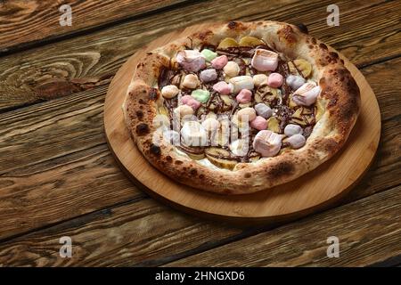 Pizza dolce intera servita con marshmallows e caramelle su sfondo di legno Foto Stock