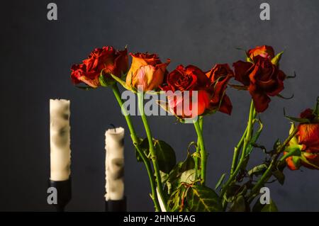 rose rosse sbiadite, una composizione di candele e fiori su sfondo grigio scuro Foto Stock