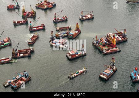 Aereo da elicottero che mostra chiatte sul Victoria Harbour carico e scarico contenitori di spedizione a metà flusso, Hong Kong Foto Stock