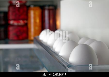 Uova di pollo crude bianche in un vassoio del frigorifero sullo sfondo dei prodotti alimentari Foto Stock