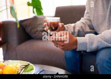 Le mani di un uomo che digita su uno smartphone mentre beve il caffè Foto Stock