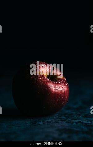 Mela Dabinet rosso fresco con gocce d'acqua in scena scura e moody. Luce straordinaria Foto Stock