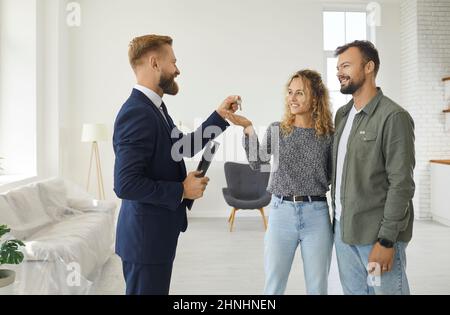 L'agente immobiliare o immobiliare dà le chiavi a casa nuova o appartamento alla famiglia giovane Foto Stock