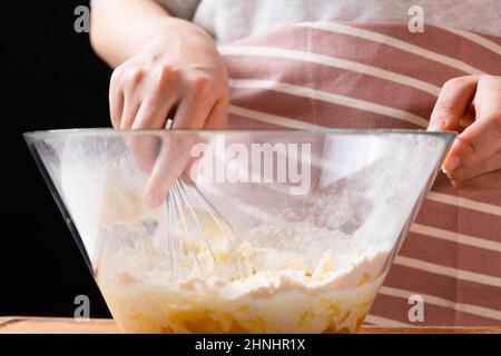 Primo piano delle mani del panettiere della donna impastando l'impasto nel recipiente di miscelazione. Pasticceria fatta in casa per torte o biscotti. Foto Stock