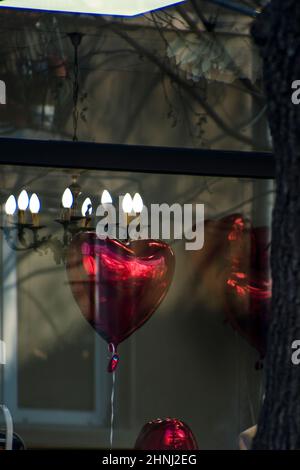 Palloncino a cuore rosso in una vetrina per celebrare il giorno di San Valentino. Lampadario chiaro sullo sfondo. Romantico giorno d'amore. Foto di alta qualità Foto Stock