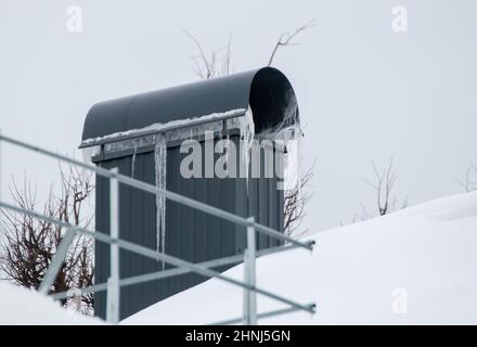 Moderno camino rettangolare in metallo sul tetto della casa. Sulla superficie c'è neve bianca. Sullo sfondo di un cielo grigio. Nuvoloso giorno d'inverno, luce tenue. Foto Stock